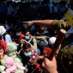 Un poliziotto ordina a centinaia di persone di mettersi in fila per prendere gli autobus Un poliziotto ordina a centinaia di persone di mettersi in fila per prendere gli autobus