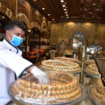 Un venditore che indossa la mascherina sul viso posiziona dei dolci sul bancone del negozio a Damasco, in Siria Un venditore che indossa la mascherina sul viso posiziona dei dolci sul bancone del negozio a Damasco, in Siria