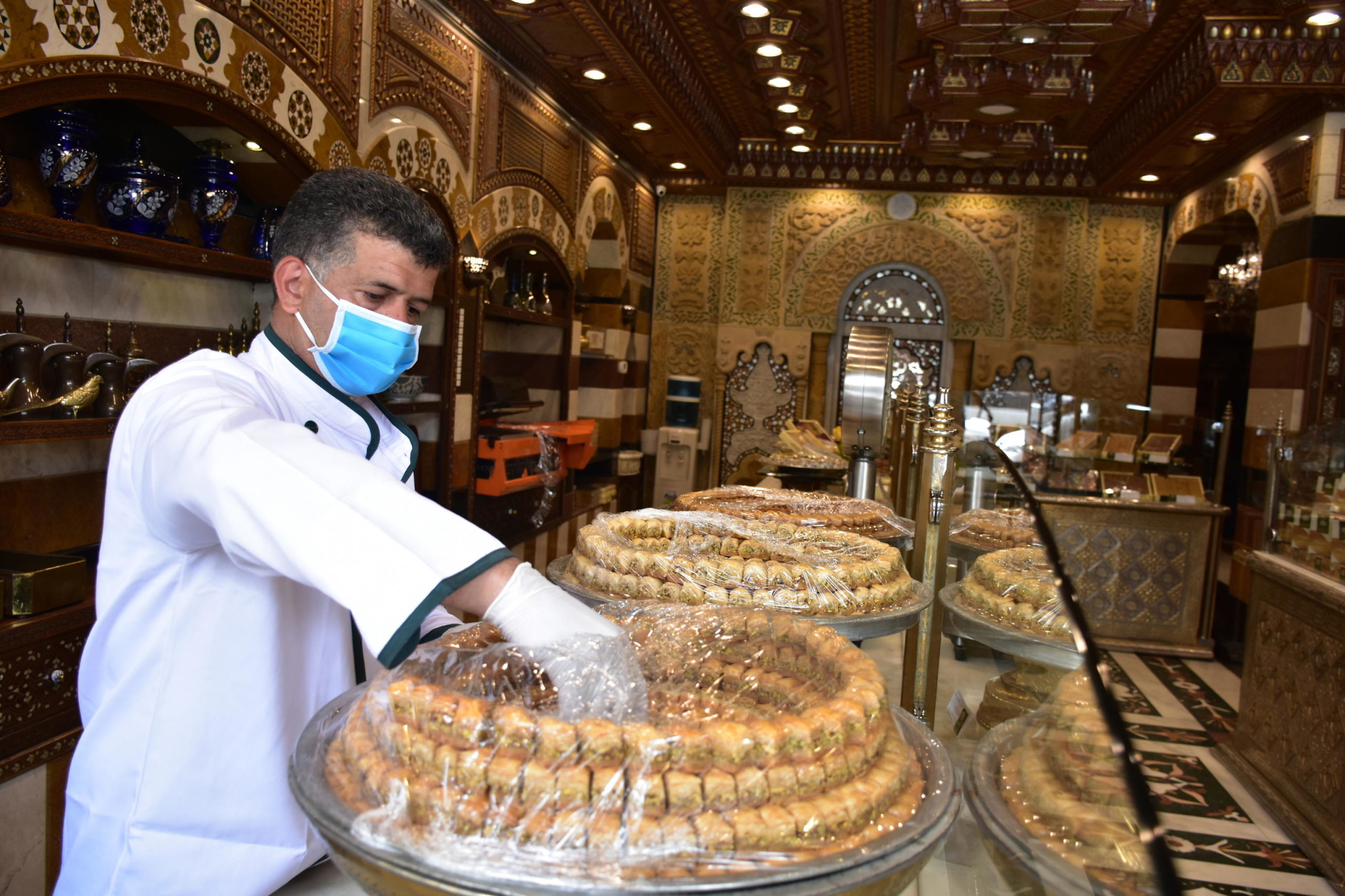 Un venditore che indossa la mascherina sul viso posiziona dei dolci sul bancone del negozio a Damasco, in Siria