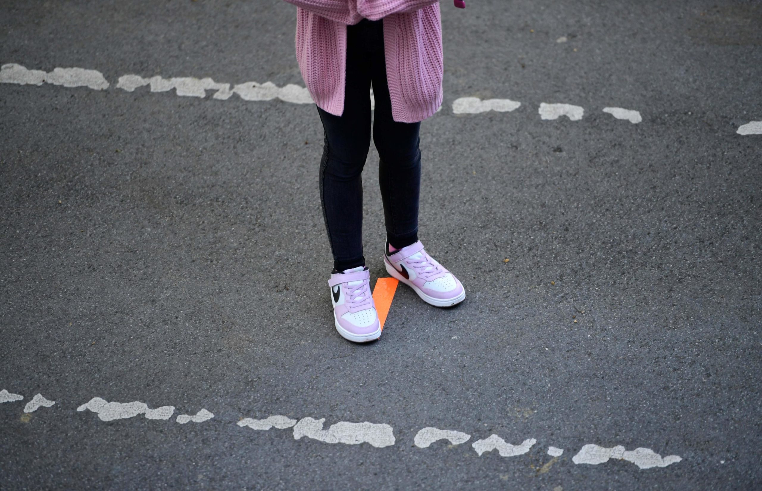 Una bambina sta in piedi sulla linea disegnata per rispettare la fila. Tutti gli alunni sono muniti di mascherine come da protocollo