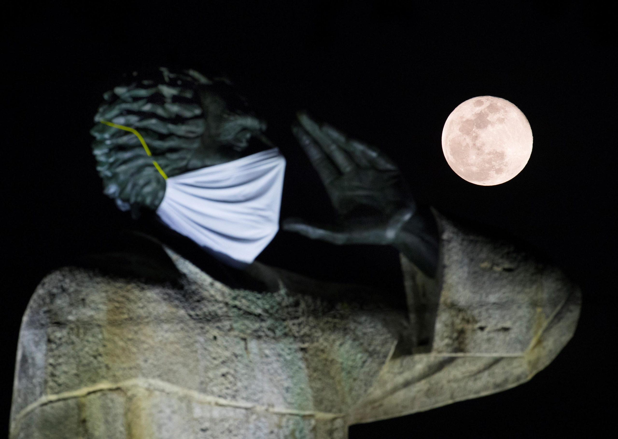 La "Luna dei fiori" splende alle spalle della statua del prete Antonio Montesino, che indossa una mascherina anti Coronavirus a Santo Domingo, nella Repubblica Domenicana