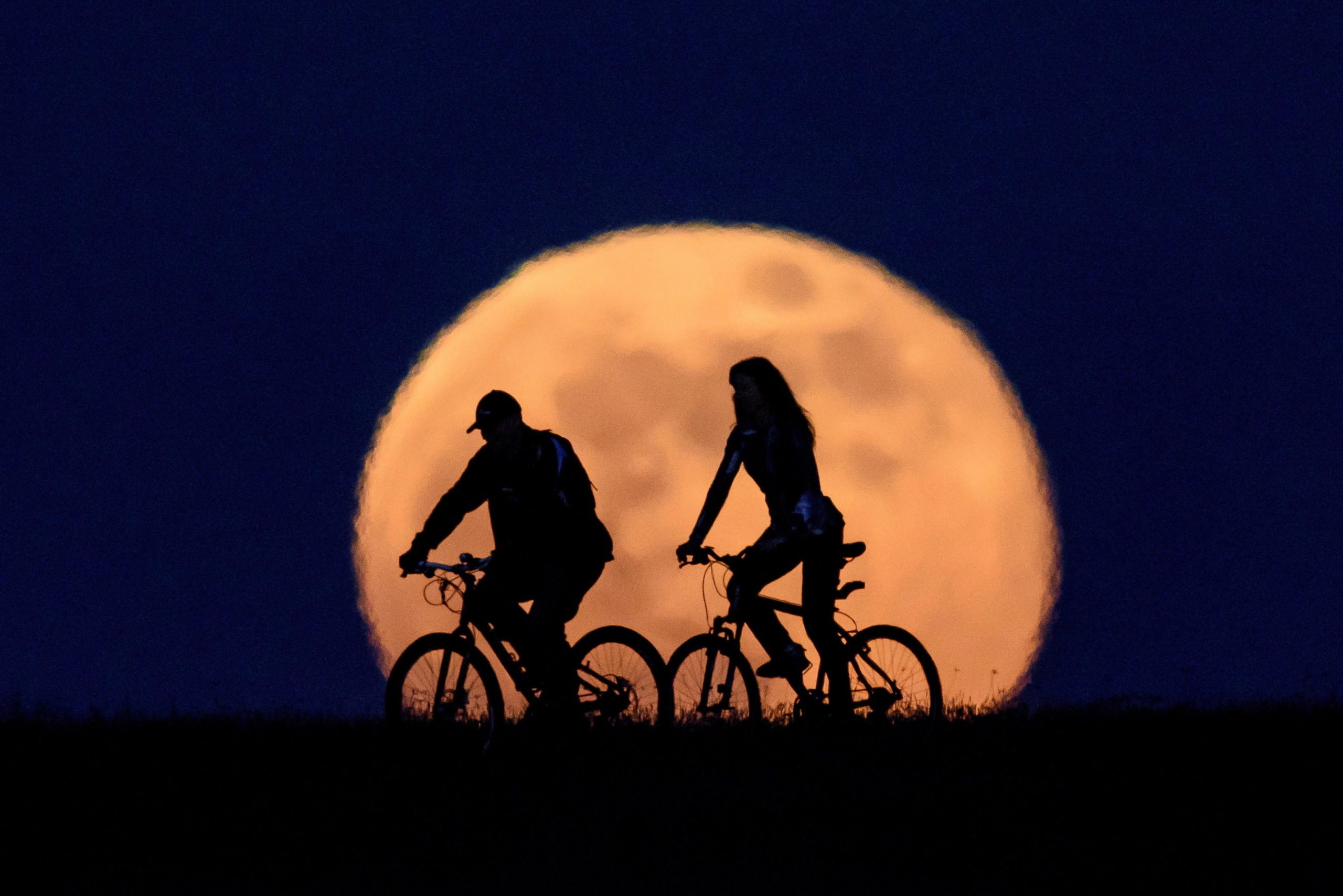 Una coppia di ciclisti pedala con la "Luna dei fiori" sullo sfondo a Salgotarjan, in Ungheria