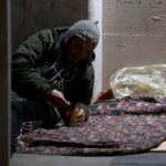 Un senzatetto apre una scatola per mangiare