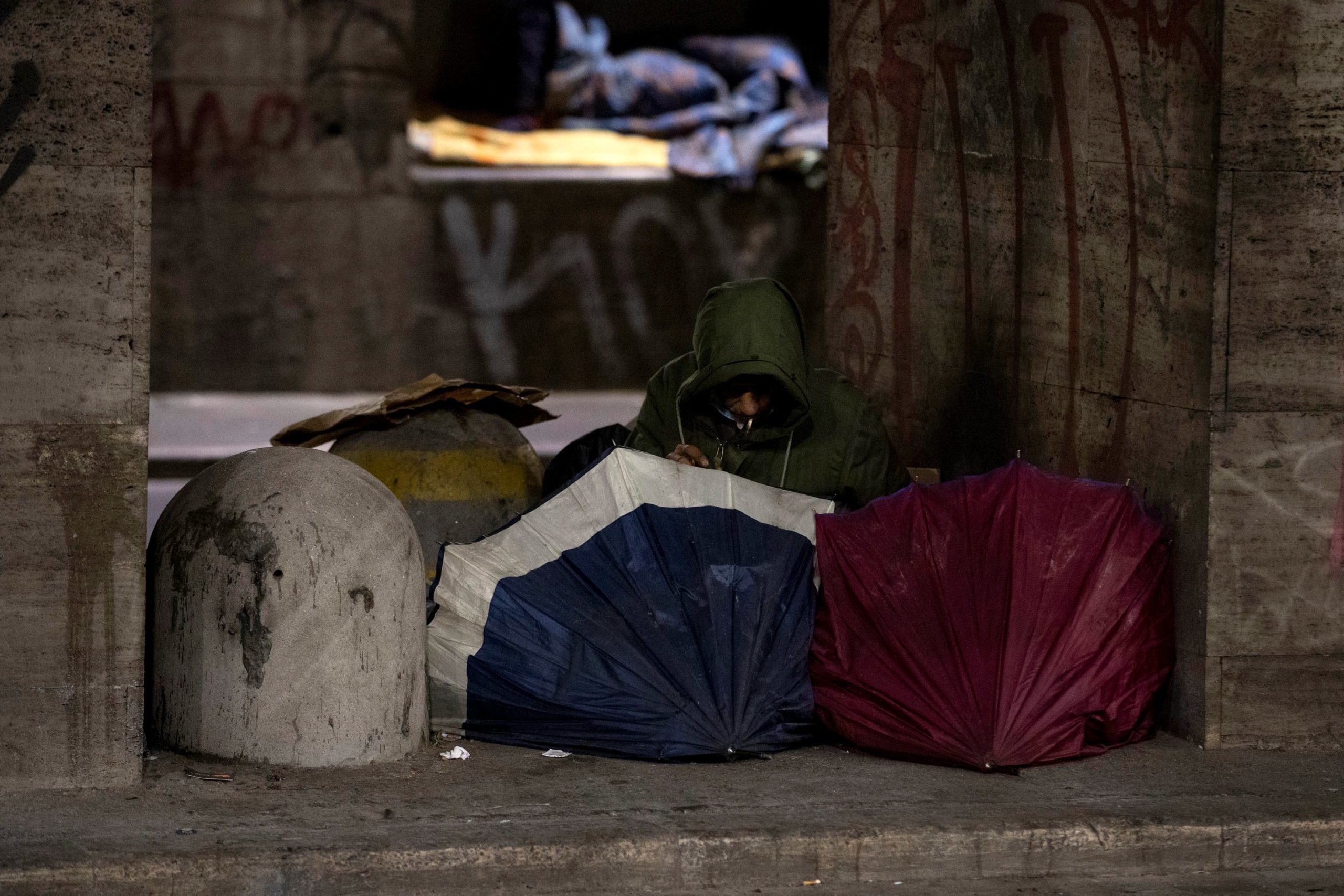 Un senzatetto si copre con degli ombrelli