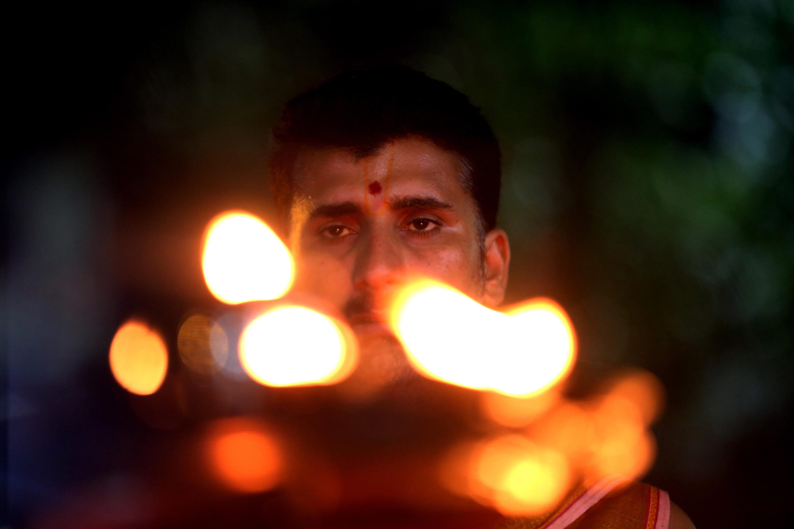 Il volto di un sacerdote induista dietro le luci delle piccole fiaccole