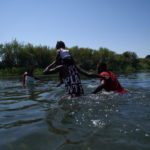 Un padre attraversa il fiume con la propria figlia sulle spalle