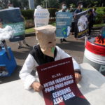Un'attivista indonesiana indossa una maschera di protesta e tiene il suo poster che recita "Le foreste dell'Indonesia non sono i polmoni del mondo, ma i camini del mondo"