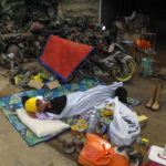 Un uomo con una coperta dorme fuori la sua casa inagibile a causa del fango. Con sé acqua e pochi viveri