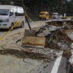 Veicoli guidano su una strada fortemente danneggiata dalle correnti del fiume