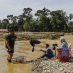Uomini e donne utilizzano il fiume per lavare i panni dopo che le forniture di acqua ed elettricità sono state tagliate a seguito dell'inondazione