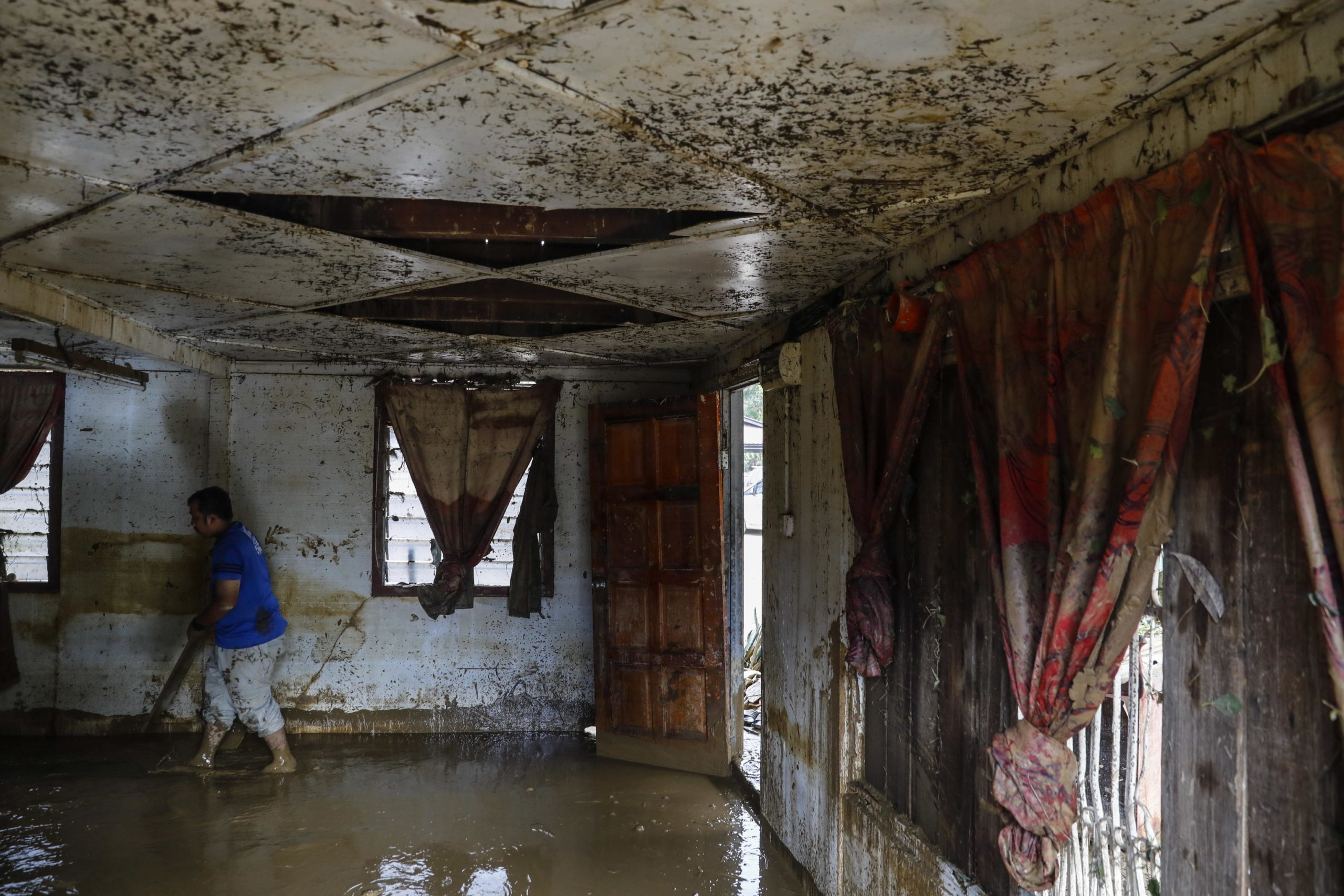 Un uomo pulisce la sua casa ricoperta di fango dopo l'alluvione