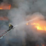 Una nuvola di fumo e detriti avvolge il vigile del fuoco mentre spegne le fiamme Una nuvola di fumo e detriti avvolge il vigile del fuoco mentre spegne le fiamme