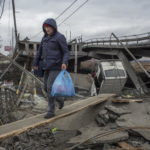 I civili attraversano le macerie di un ponte danneggiato nella città di Irpin vicino a Kiev