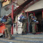 Poliziotti ucraini e militari del Comando di difesa territoriale trasportano merci da un negozio danneggiato per metterle al sicuro dopo i bombardamenti a Kharkiv