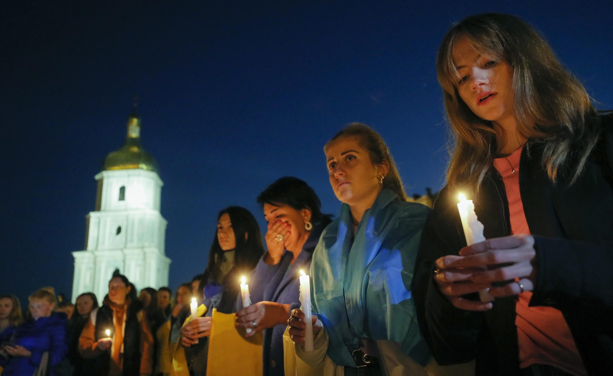 Diverse persone reggono candele accese in memoria delle vittime del centro di Olenivka