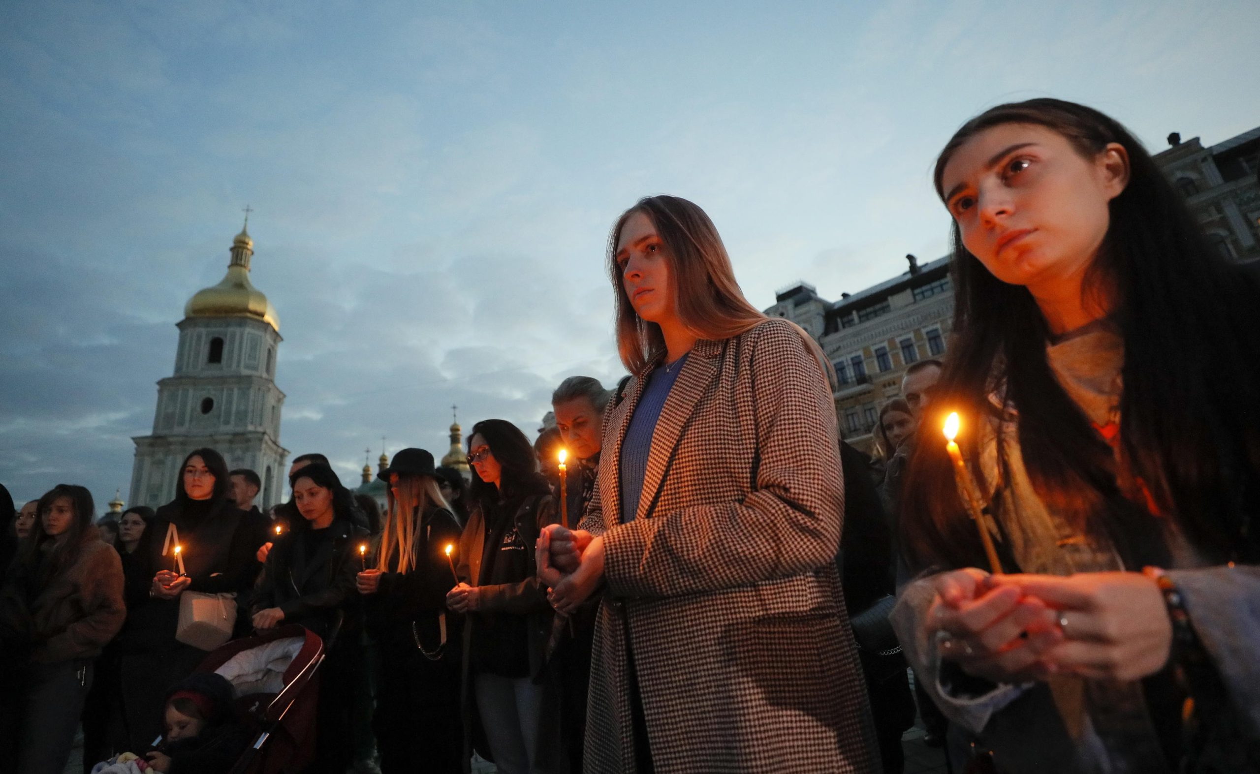 Diverse persone reggono candele accese in memoria delle vittime del centro di Olenivka