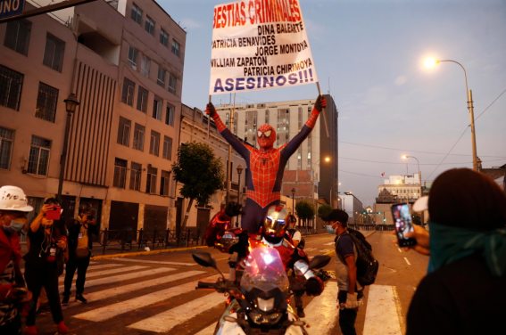 Due manifestanti vestiti da supereroi espongono un cartellone critico nelle strade di Lima