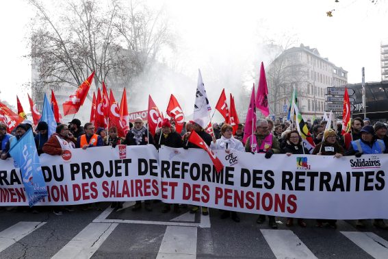 Manifestanti marciano tenendo uno striscione con la scritta "ritiro della riforma pensionistica"