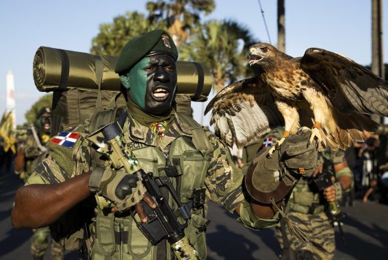 Un militare domenicano partecipa alla parata militare, con una mano tiene un'arma, con l'altra un falco