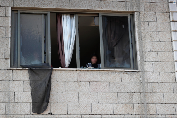 Una ragazza palestinese si affaccia alla finestra della sua casa danneggiata