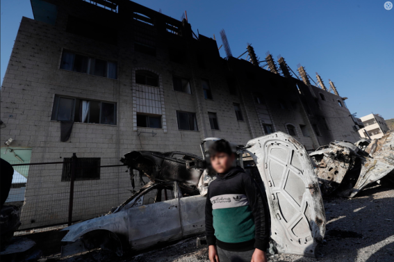 Un ragazzo palestinese tra le auto bruciate accanto alla sua casa