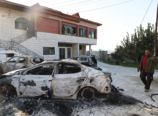 Un uomo cammina vicino a un edificio danneggiato e ad auto bruciate