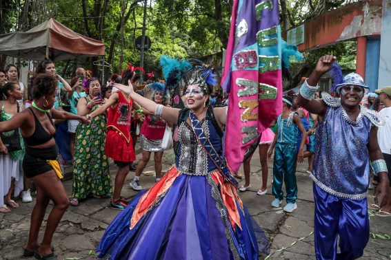 Una donna in abiti carnevaleschi sfila per le strade di Rio, intorno a lei una folla danzante di partecipanti