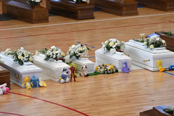 Una fila di bare bianche, con sopra corone di fiori, peluche e giocattoli per i bambini scomparsi nella tragedia di Cutro