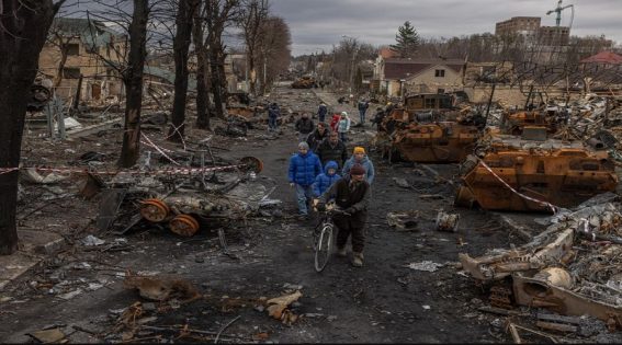 Abitanti di Bucha camminano tra i resti dei macchinari militari russi, 6 aprile 2022.