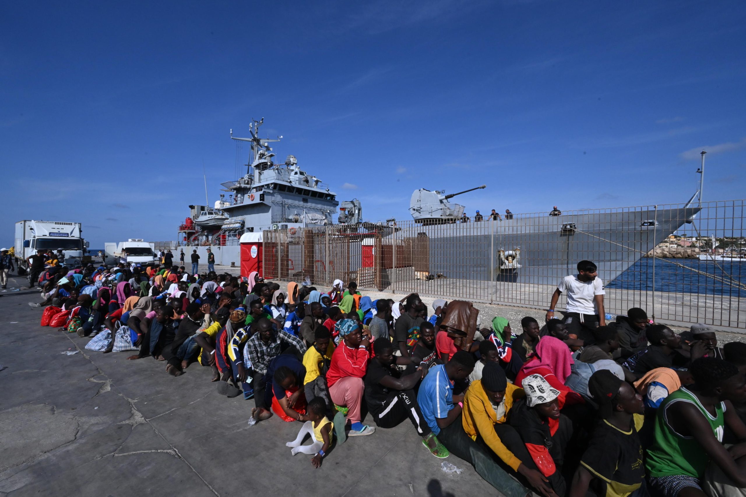 Centinaia di migranti aspettano in fila al molo del porto per essere imbarcati sulla nave militare Cassiopea