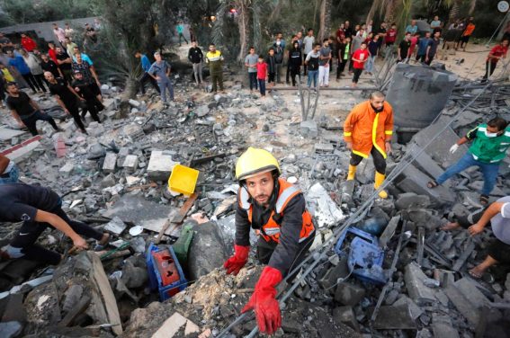 Soccorritori e civili palestinesi rimuovono le macerie di un edificio distrutto dopo un attacco israeliano alla città di Deir Al-Balah