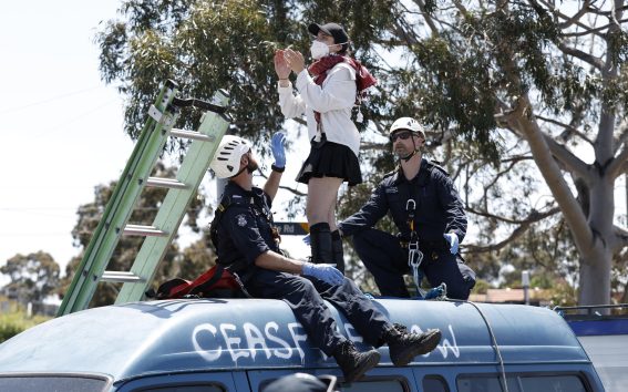 Una manifestante protesta sopra un furgone mentre due poliziotti le intimano di scendere a Melbourne
