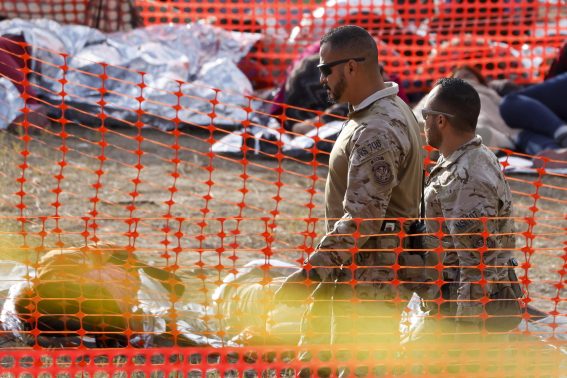 Agenti della dogana passano accanto a migranti sdraiati sul terreno dello Shelby Park di Eagle Pass, Texas, USA Agenti della dogana passano accanto a migranti sdraiati sul terreno dello Shelby Park di Eagle Pass, Texas, USA