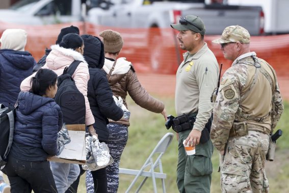 Migranti passano davanti a un agente della polizia di frontiera e a una guardia nazionale del Texas allo Shelby Park di Eagle Pass, Texas, USA