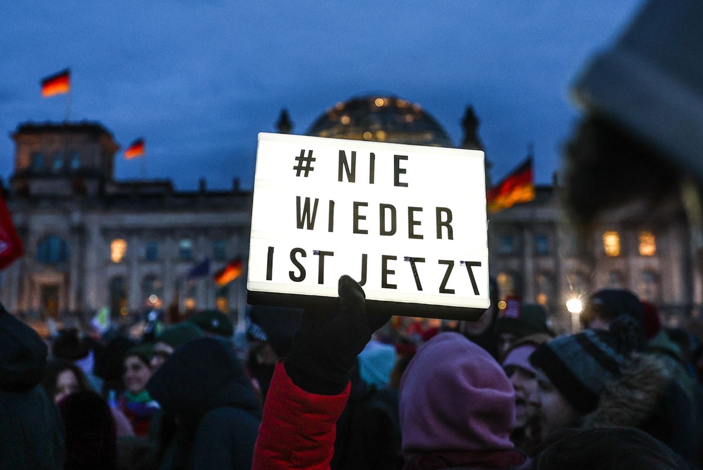 Un manifestante mostra un cartello con la scritta "mai più è ora" davanti al Parlamento tedesco