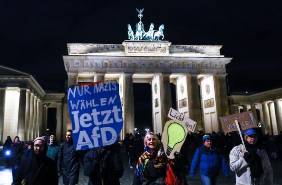 Alcuni manifestanti espongono cartelli mentre camminano davanti alla Porta di Brandeburgo