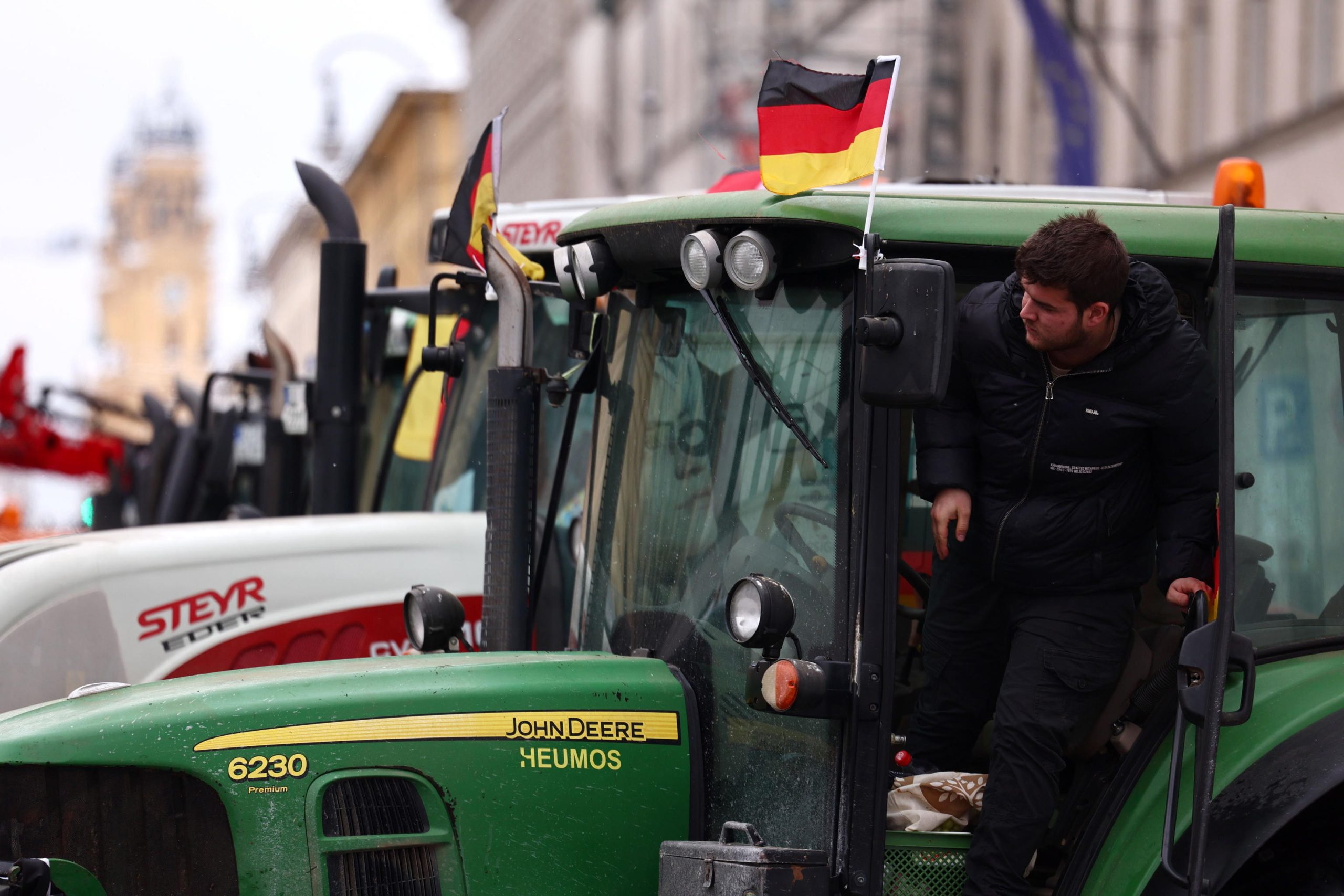 Un contadino si sporge dal proprio trattore, da cui sventola un tricolore tedesco.