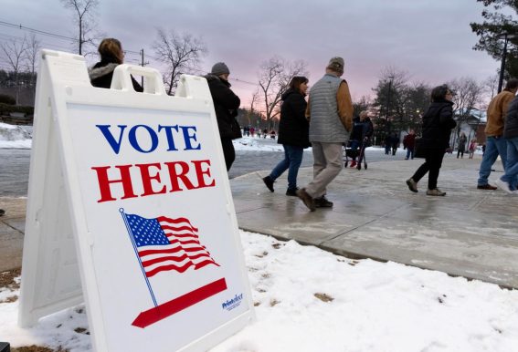 Il segnale "Vota qui" fuori dalla Pinkerton Academy a Derry, sullo sfondo le persone vanno a votare
