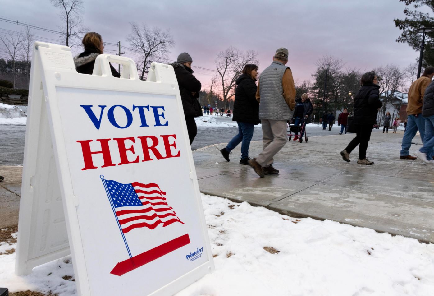 Il segnale "Vota qui" fuori dalla Pinkerton Academy a Derry, sullo sfondo le persone vanno a votare