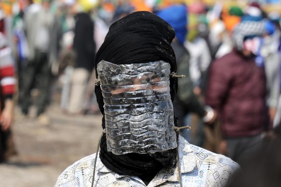 Un agricoltore in protesta ha il volto coperto per proteggersi dai gas lacrimogeni sparati dalla polizia indiana