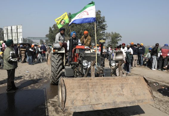 Agricoltori del Punjabi tengono bandiere seduti in cima al loro veicolo durante la protesta