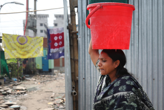 Una donna trasporta acqua in una bacinella tenendola in equilibrio sulla testa in Bangladesh