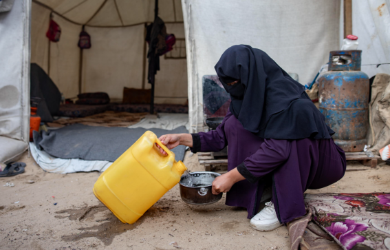 Una donna palestinese versa l'acqua da un contenitore in una pentola nel suo rifugio a Khan Yunis, nel sud della Striscia di Gaza