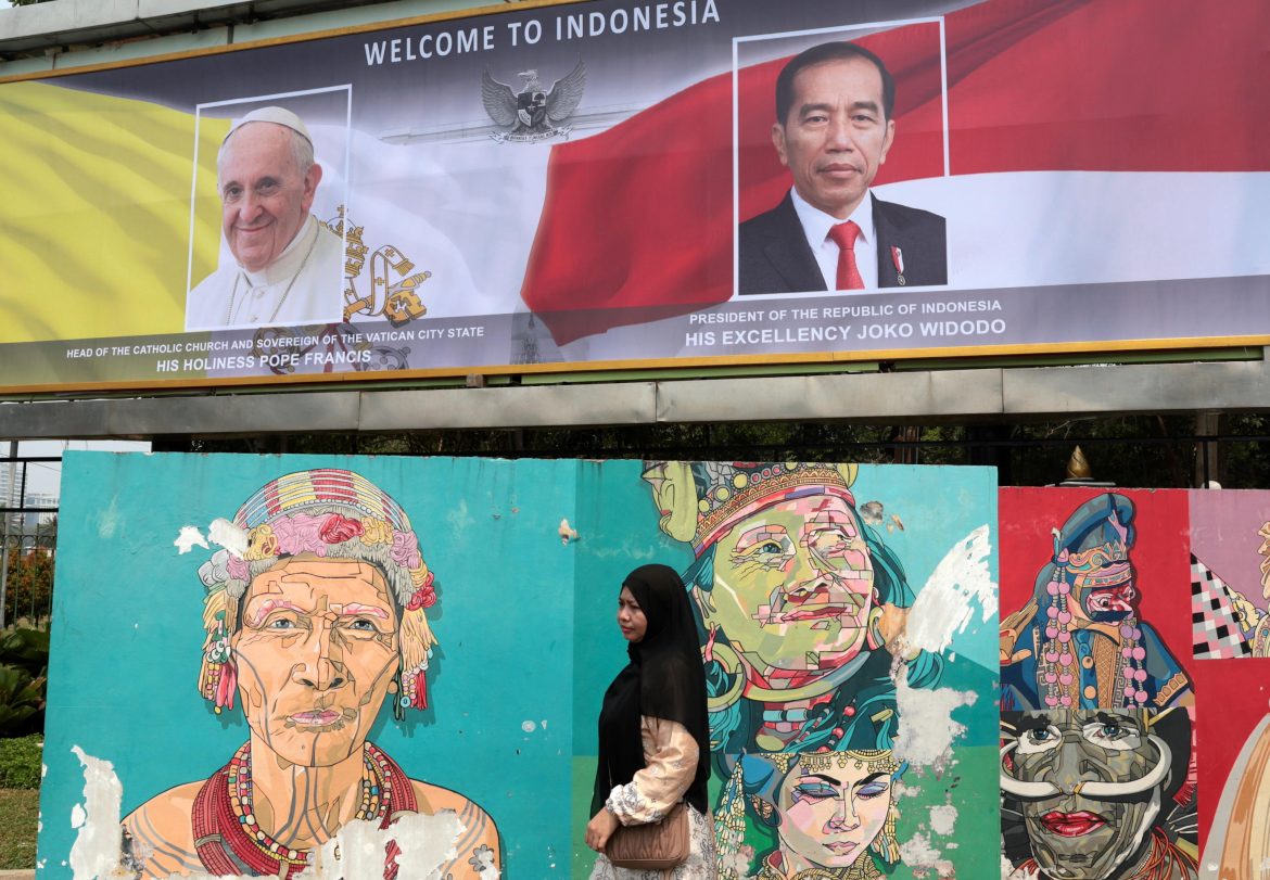 Una donna musulmana passa davanti a un banner raffigurante Papa Francesco e il presidente indonesiano Joko Widodo