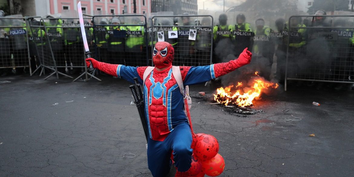 Ecuador-10 Un manifestante si mostra vestito da Spiderman davanti al blocco della polizia ecuadoregna per impedire l'arrivo della marcia di protesta al palazzo presidenziale, mentre una pila di pneumatici brucia | Foto Ansa