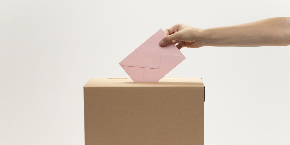 la-mano-mette-la-busta-rosa-nella-casella-di-voto (1)