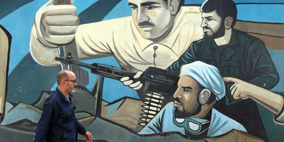 Un uomo iraniano cammina accanto a un dipinto murale raffigurante soldati iraniani a Teheran, Iran