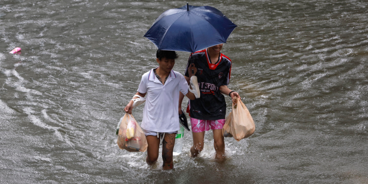 ombrello Dei residenti avanzano nell'acqua con le buste della spesa | Foto Ansa
